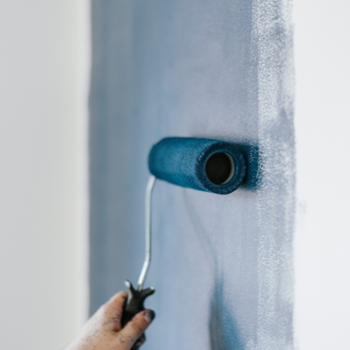 A paint roller painting an interior wall blue.